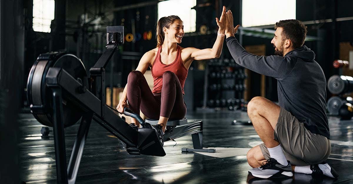 Client giving high-five to her personal trainer after exercising on rowing machine in a gym