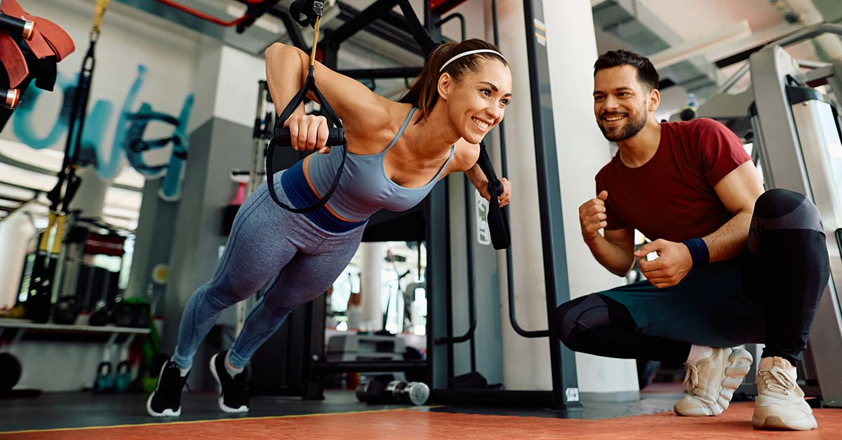 woman practicing push ups with trx straps in a gym with trainer