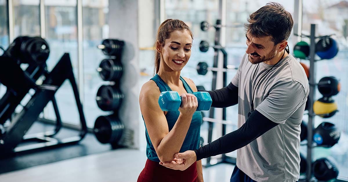 client exercising with dumbbells while personal trainer is assisting