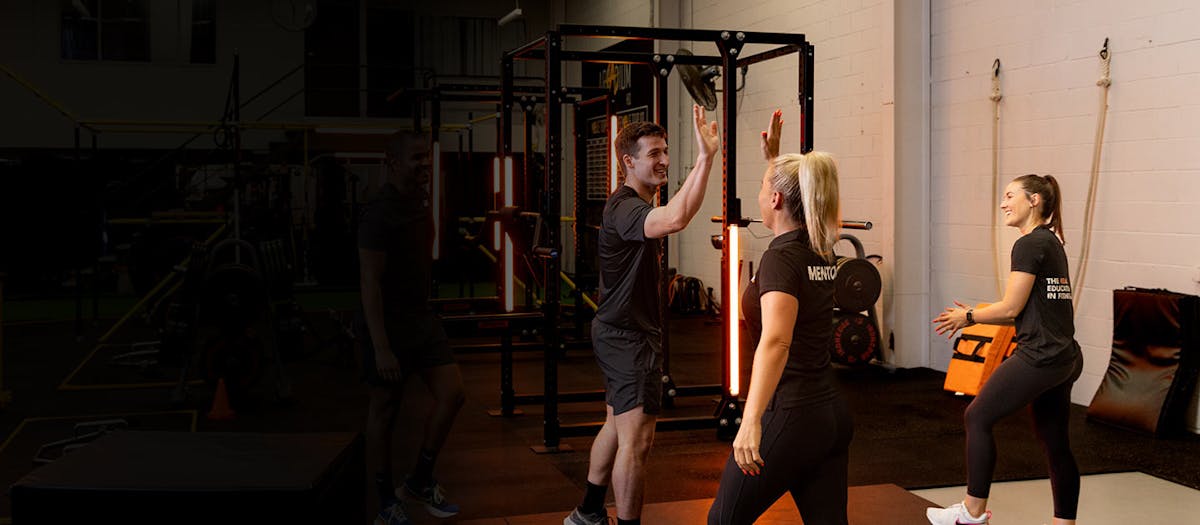 Male AIPT personal training mentor high-fiving a female student during practical in-gym fitness education training.