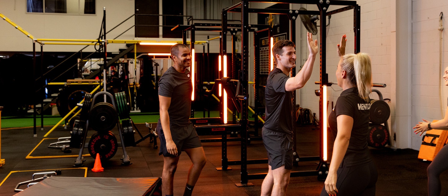 Fitness student high-fiving an AIPT mentor during practical training in a gym facility.