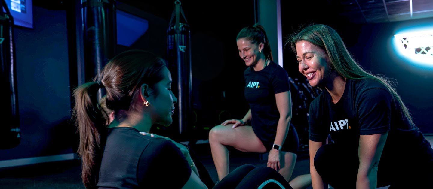 Female AIPT fitness mentors guiding a student through practical exercises during a Campus Club gym session.