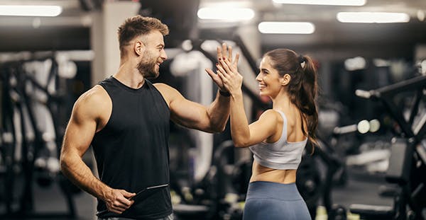 Male personal trainer high-fiving a female client during a PT consultation session in a gym.