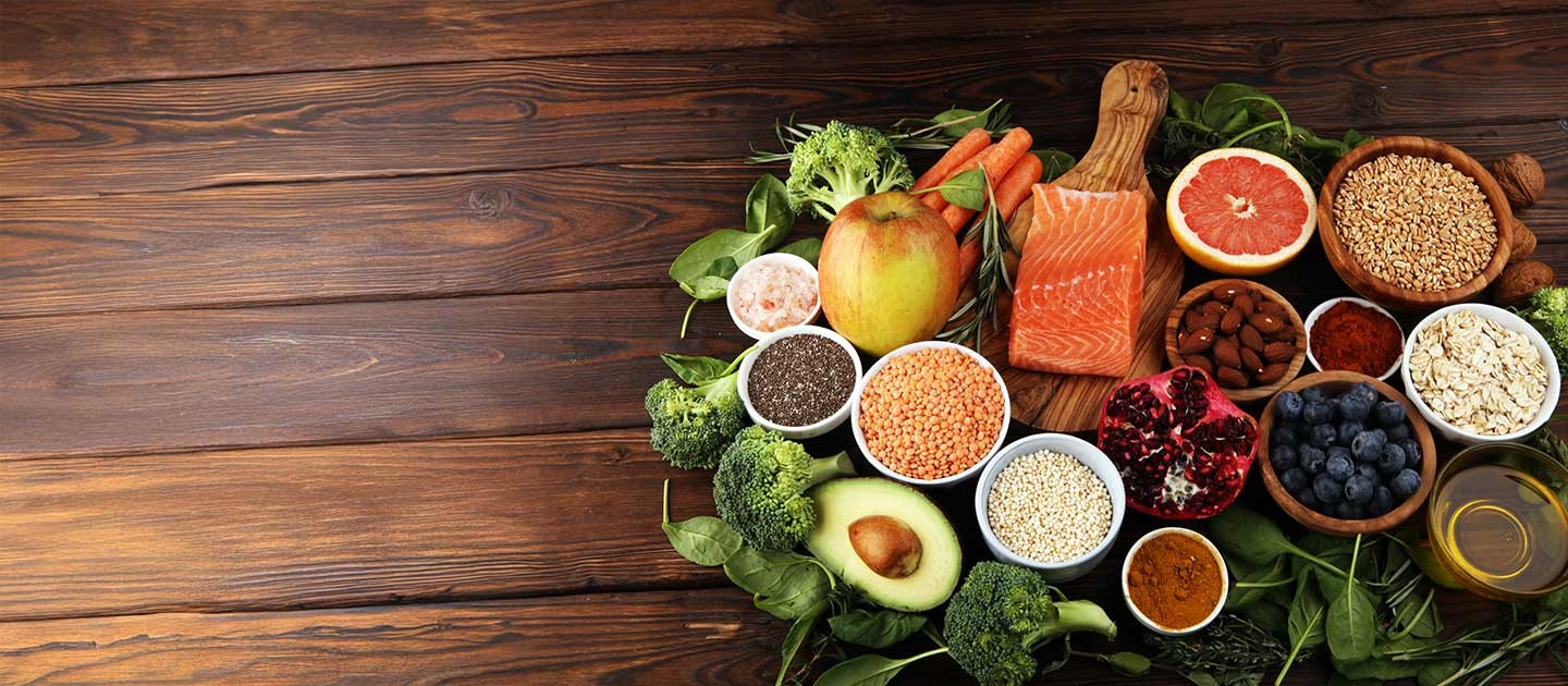Flat lay of healthy nutrition foods arranged on a wooden table for an Australian Institute of Personal Trainers (AIPT) course, featuring a piece of salmon, an apple, bowls of seeds, nuts, berries, grains, and green vegetables.