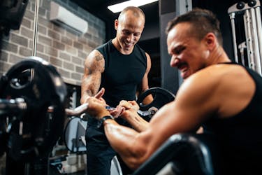 Personal trainer supporting a client during a strength training session in a gym