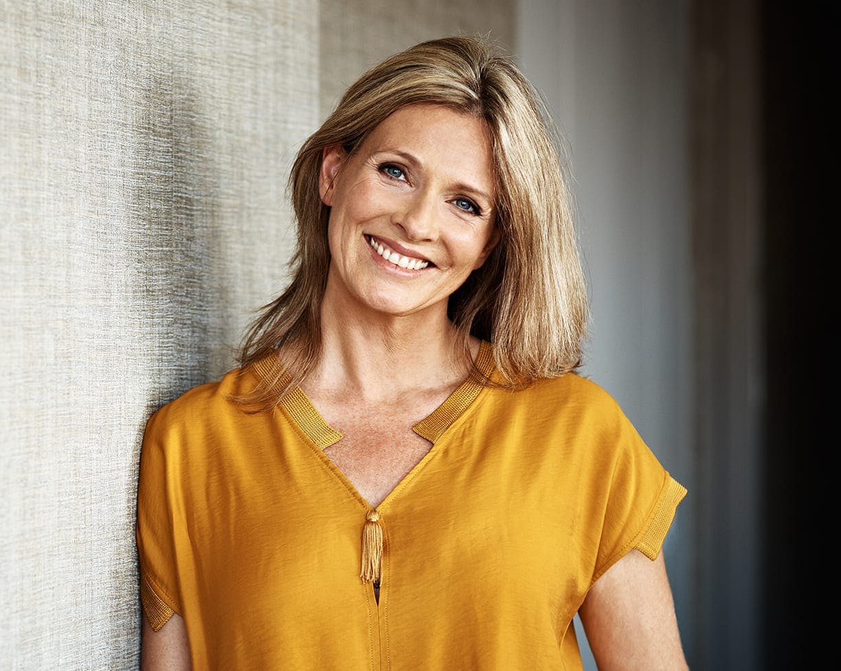 Beautiful middle aged woman smiling wearing a yellow shirt