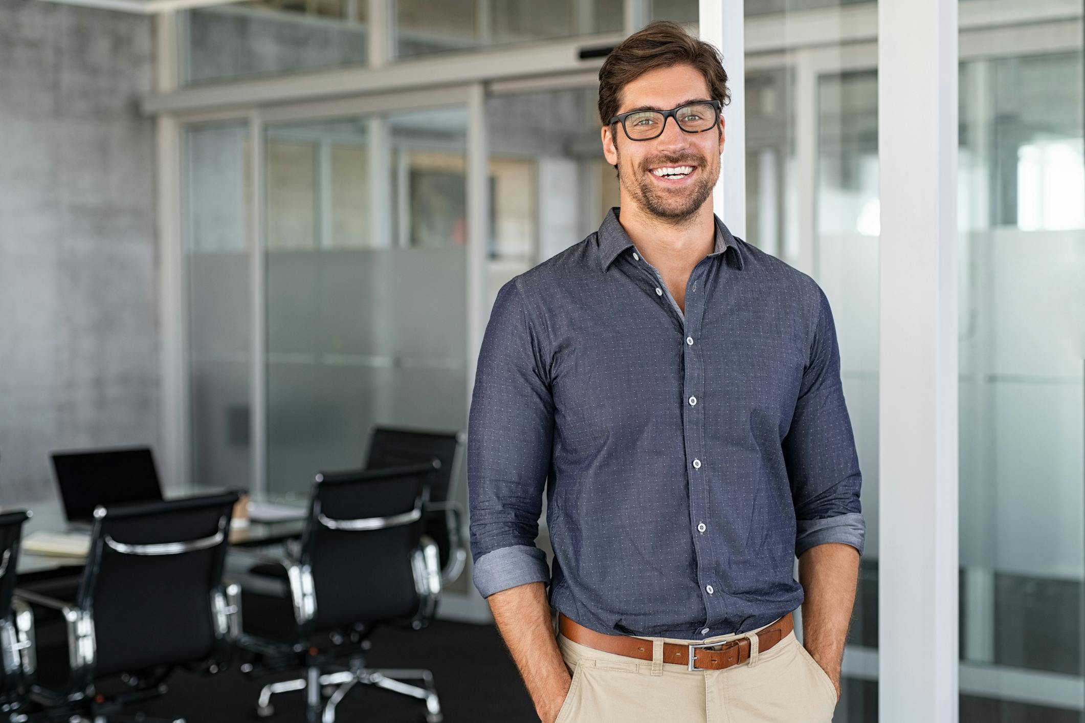 smiling man in glasses standing in an office with a laptop