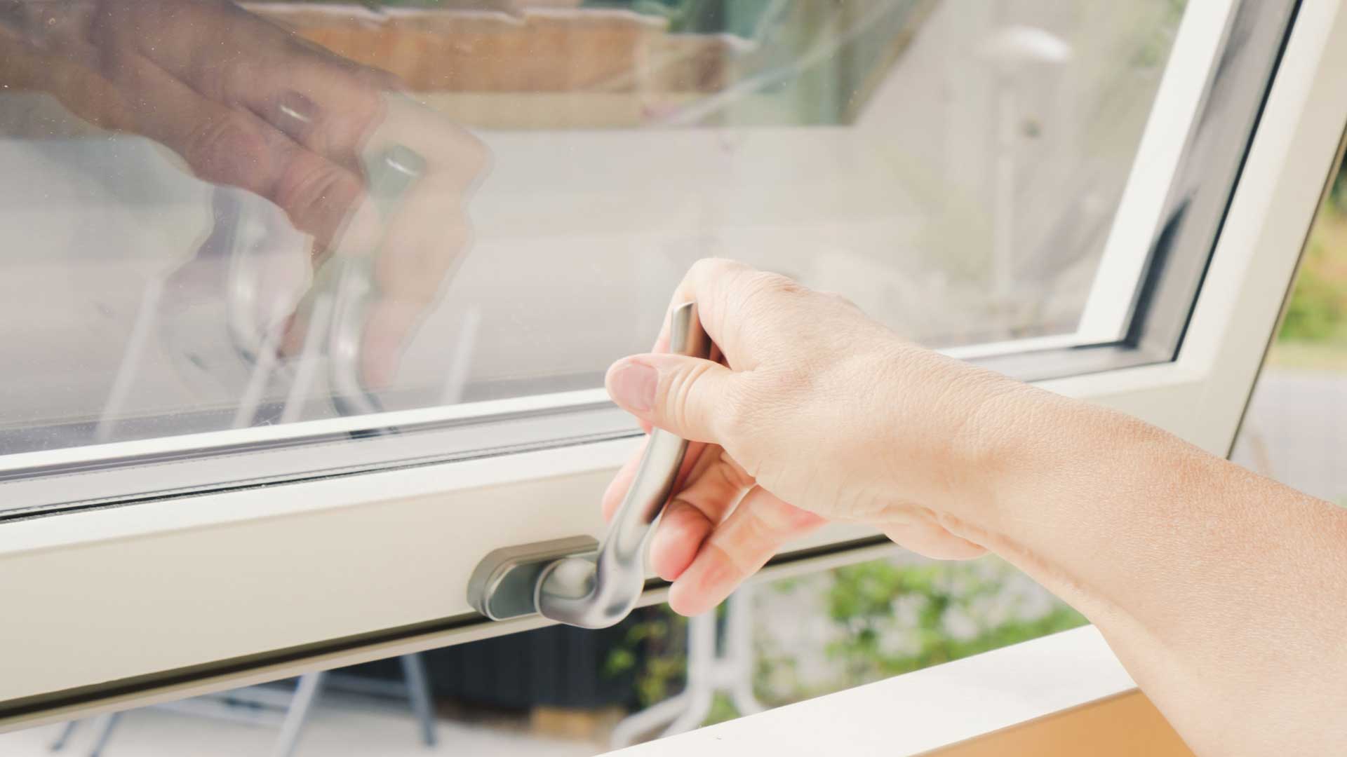 Person der åbner topstyret vindue med krom håndtag ud mod naturen