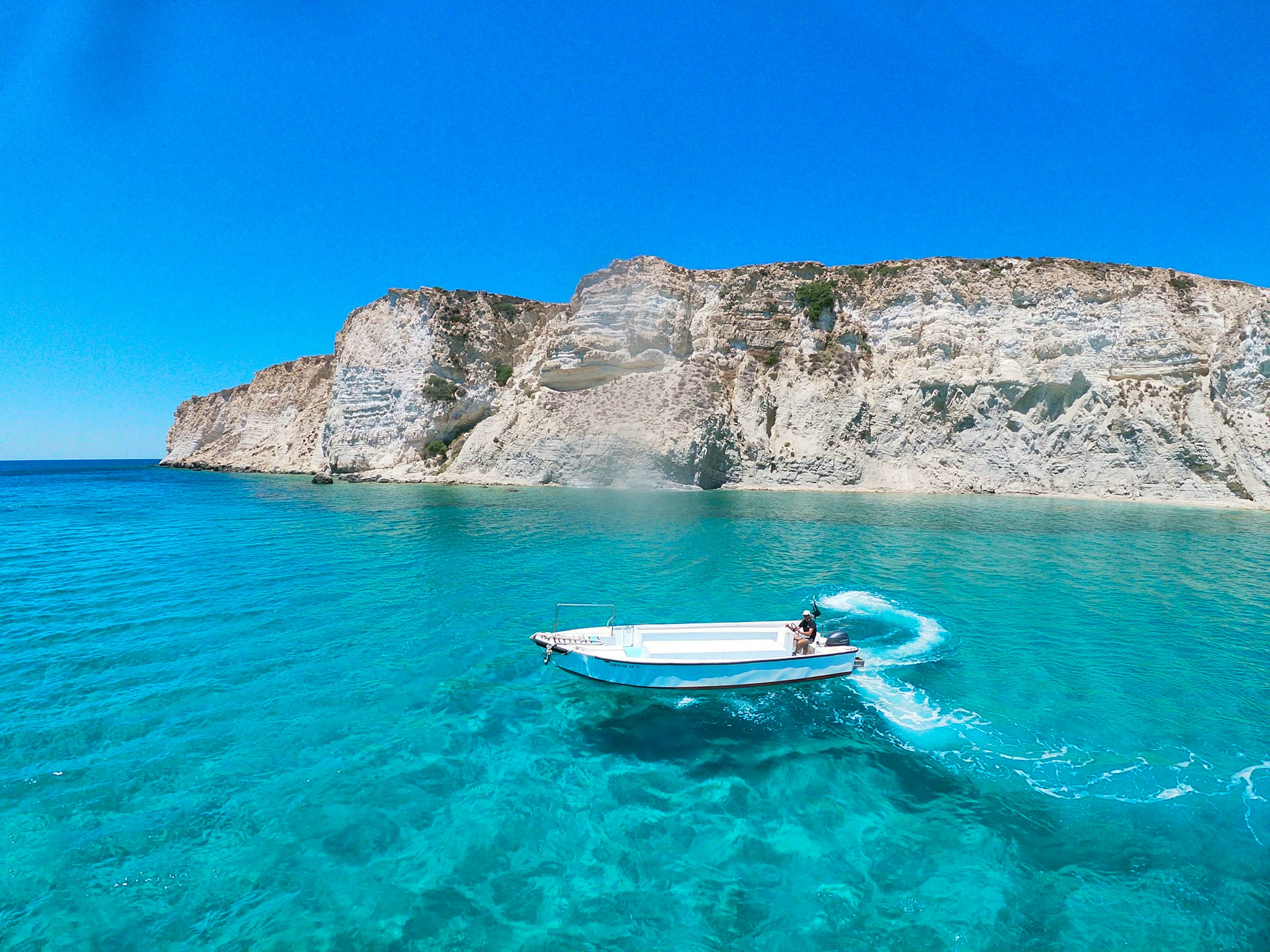 white and blue boat on blue sea near gray rocky mountain during daytime