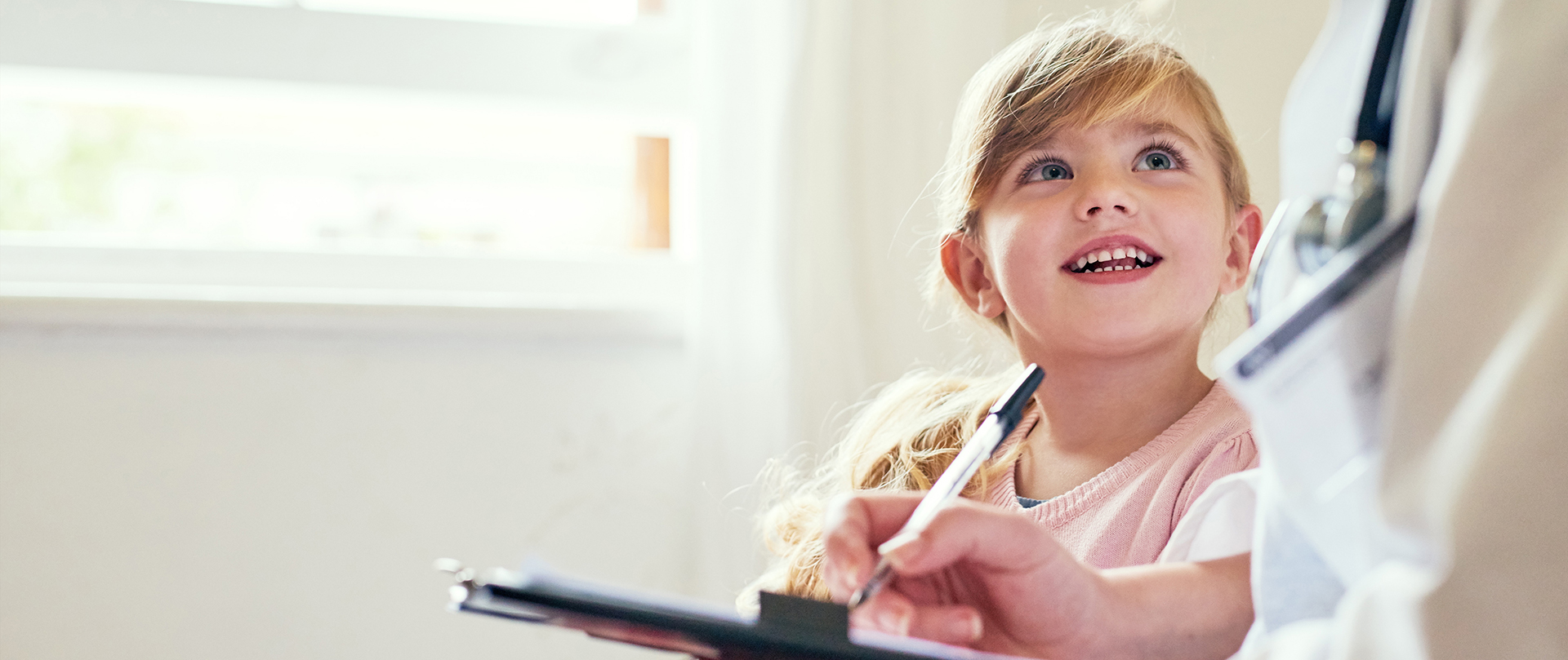 a young girl smiling up at at a doctor with clipboard