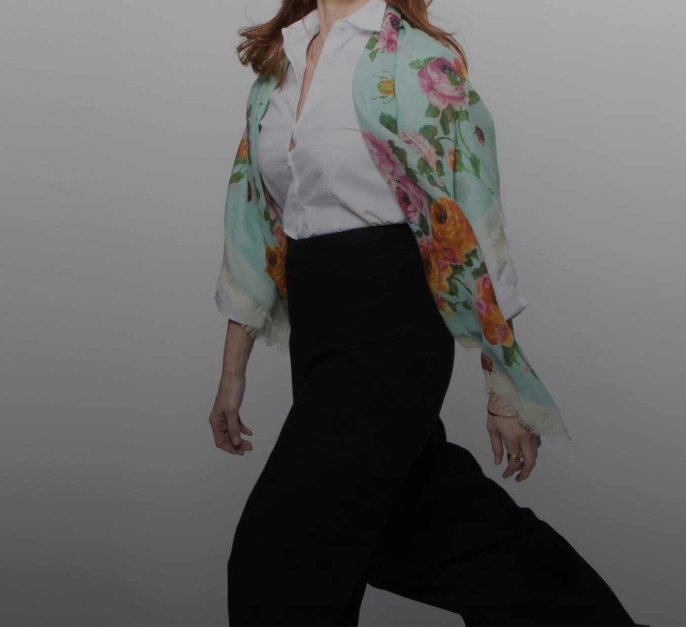 a model walking with a floral shawl, white button down, and black pants