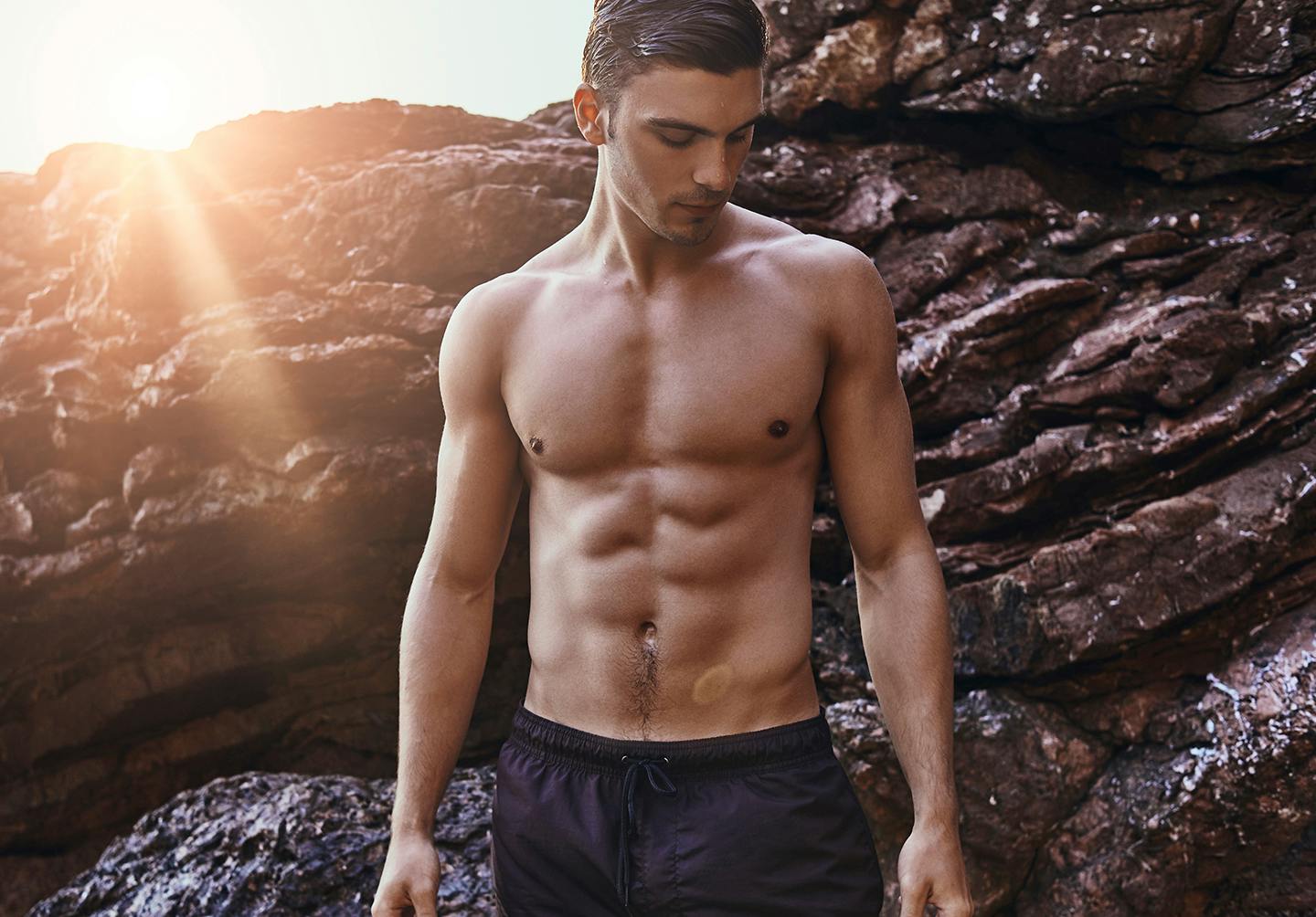 a man shirtless standing in front of larger rocks