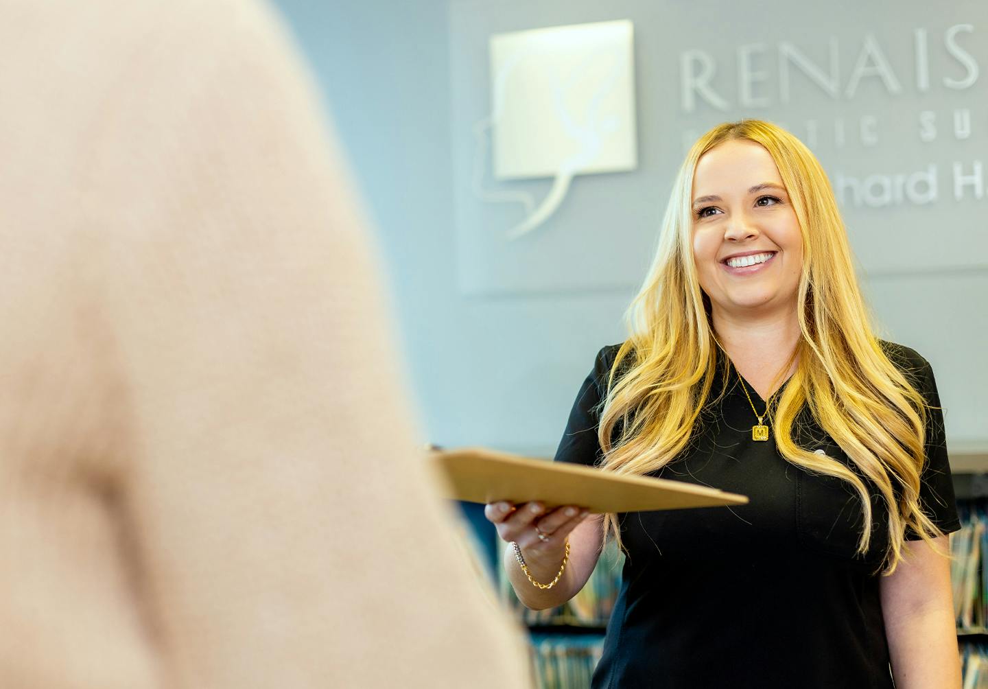 a staff member with blonde hair handing someone a folder