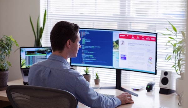 man in gray dress shirt sitting on chair in front of computer monitor