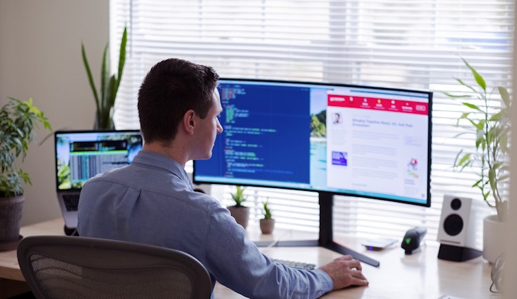 man in gray dress shirt sitting on chair in front of computer monitor