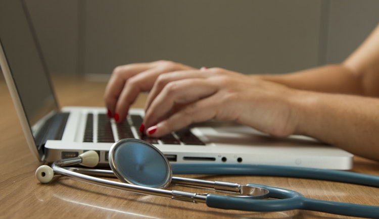 person sitting while using laptop computer and green stethoscope near