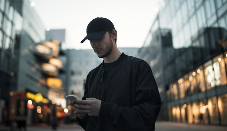 man in black jacket wearing black fitted cap while using phone