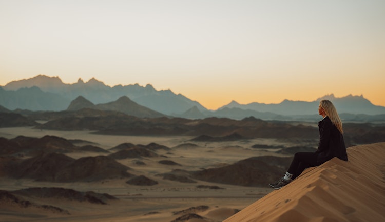 a woman sitting on top of a sand dune