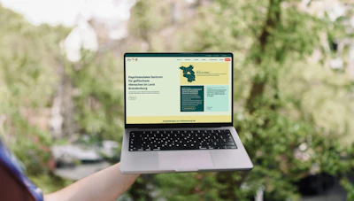 Laptop mit der neuen KommMit Webseite draußen vor grünem Hintergrund