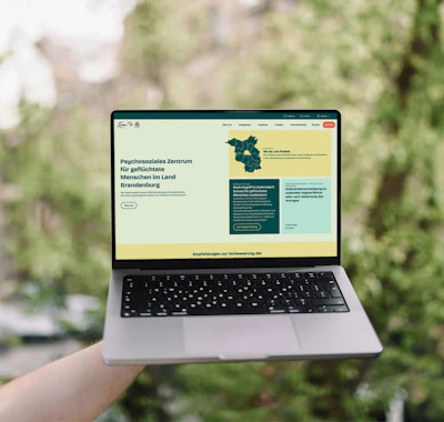 Laptop mit der neuen KommMit Webseite draußen vor grünem Hintergrund