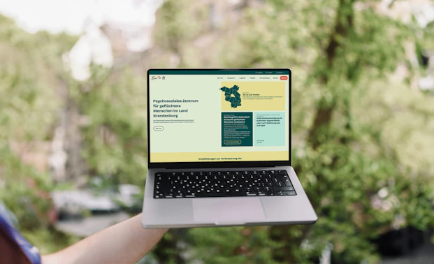 Laptop mit der neuen KommMit Webseite draußen vor grünem Hintergrund