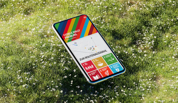 Mockup mit Smartphone auf Wiese, Screen zeigt Vorschau der 17 Ziele App der Stadt Freiburg
