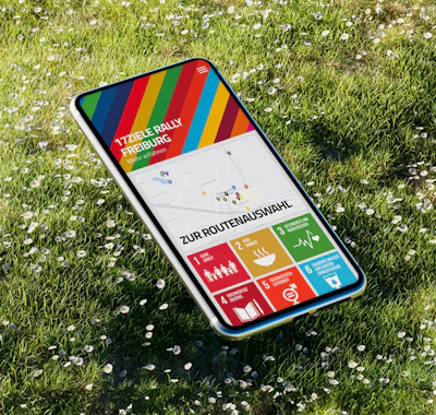 Mockup mit Smartphone auf Wiese, Screen zeigt Vorschau der 17 Ziele App der Stadt Freiburg