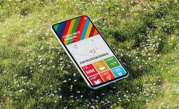 Mockup mit Smartphone auf Wiese, Screen zeigt Vorschau der 17 Ziele App der Stadt Freiburg