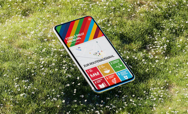 Mockup mit Smartphone auf Wiese, Screen zeigt Vorschau der 17 Ziele App der Stadt Freiburg