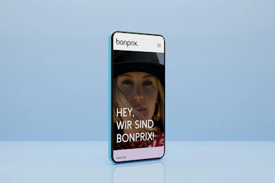Smartphone mit blauem Hintergrund zeigt die Startseite von bonprix Corporate