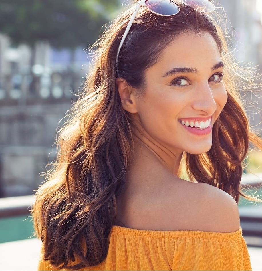 Beautiful woman with long hair and sunglasses on her head, looking back into the camera.