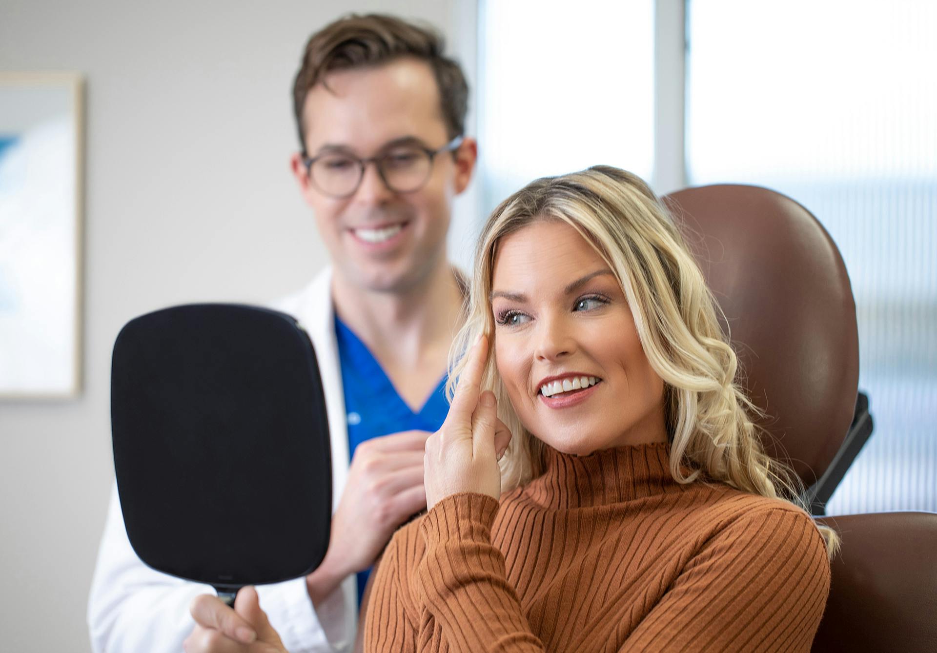 Woman looking in a handheld mirror at while with a doctor at Clevens Face and Body Specialists