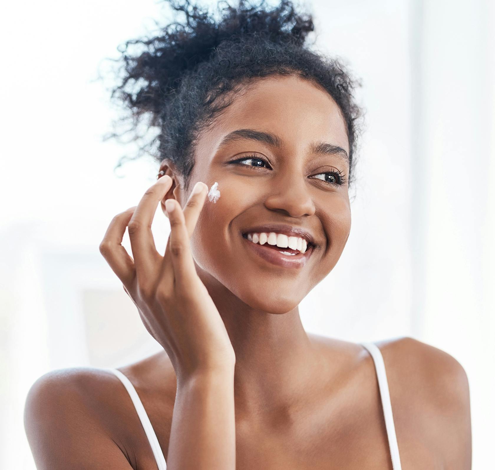 smiling woman applying cream on her face