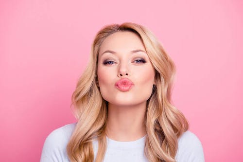 woman with blonde wavy hair puckering her lips into a kiss