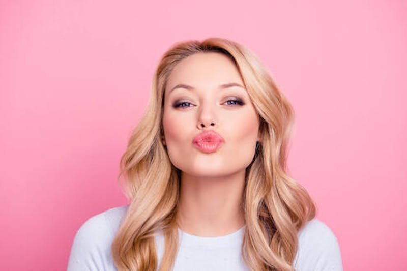 woman with blonde wavy hair puckering her lips into a kiss