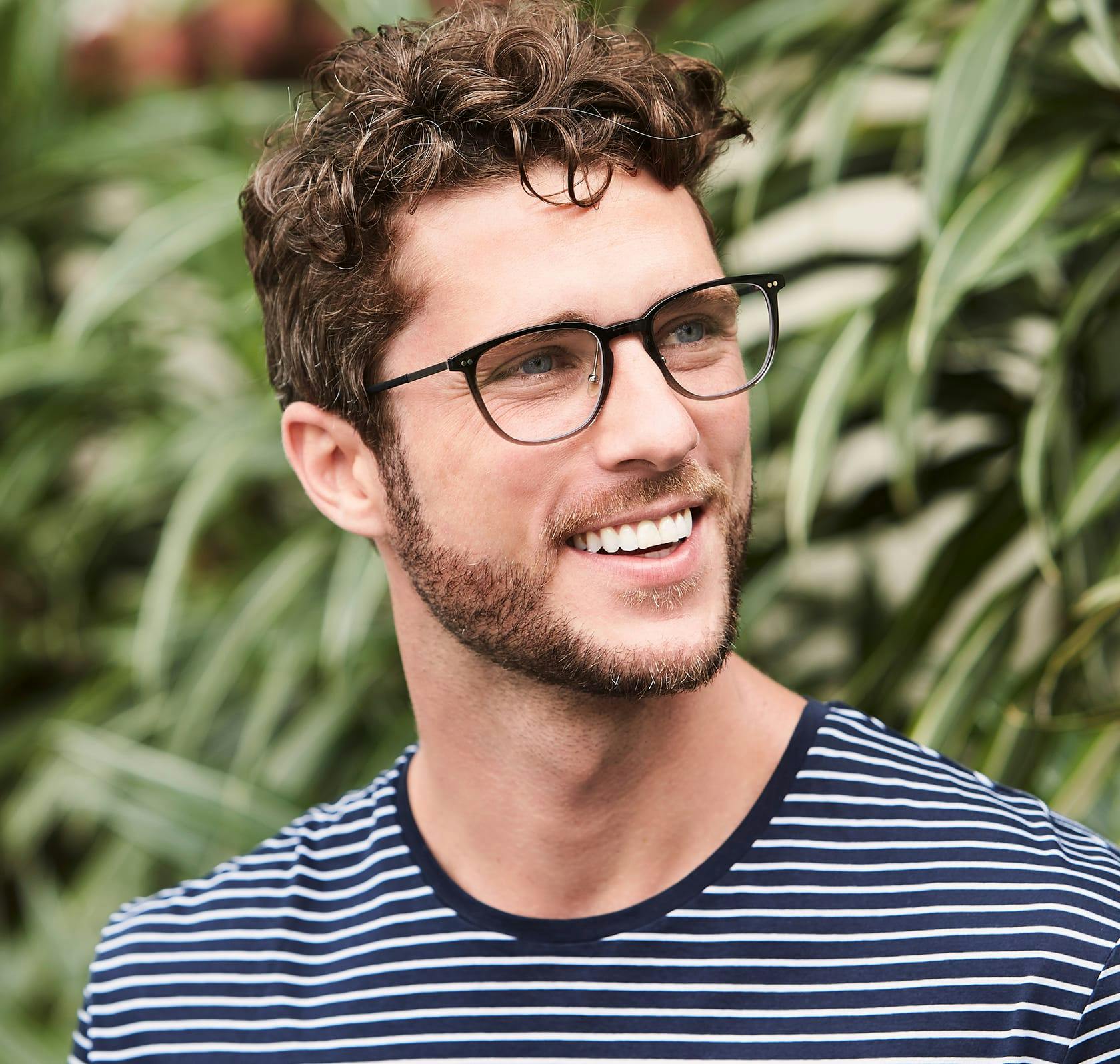 smiling man with glasses and a striped shirt in front of a bush