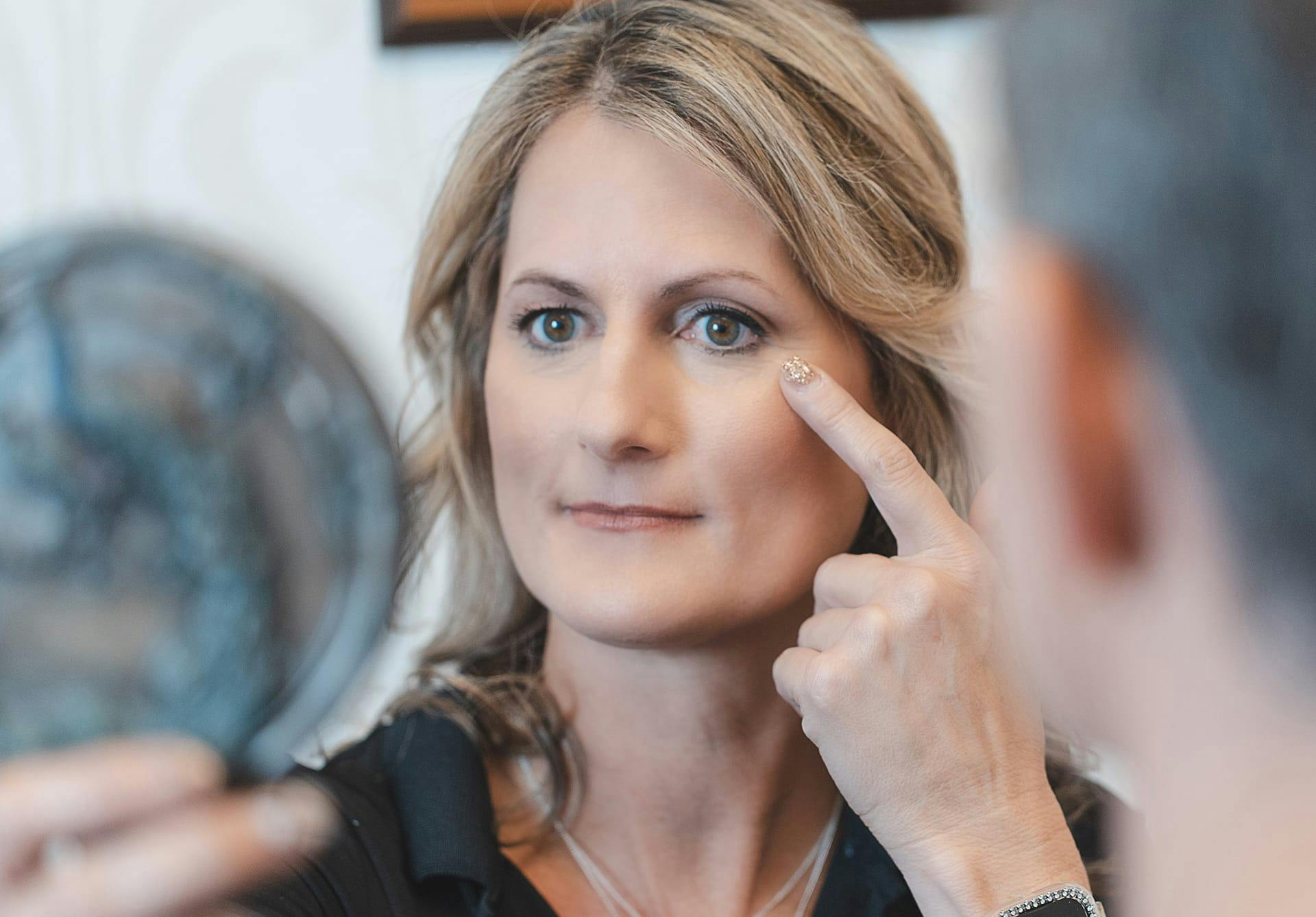 woman looking and pointing at face and holding a mirror