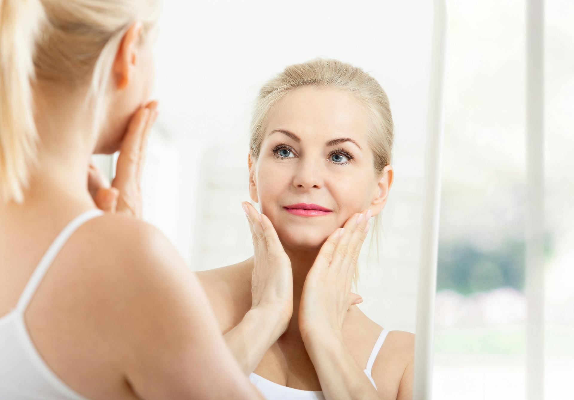 woman looking into a mirror and touching her face