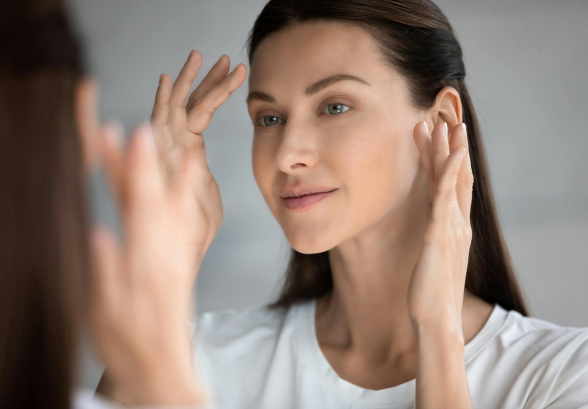 Woman looking in the mirror with her hands near her face