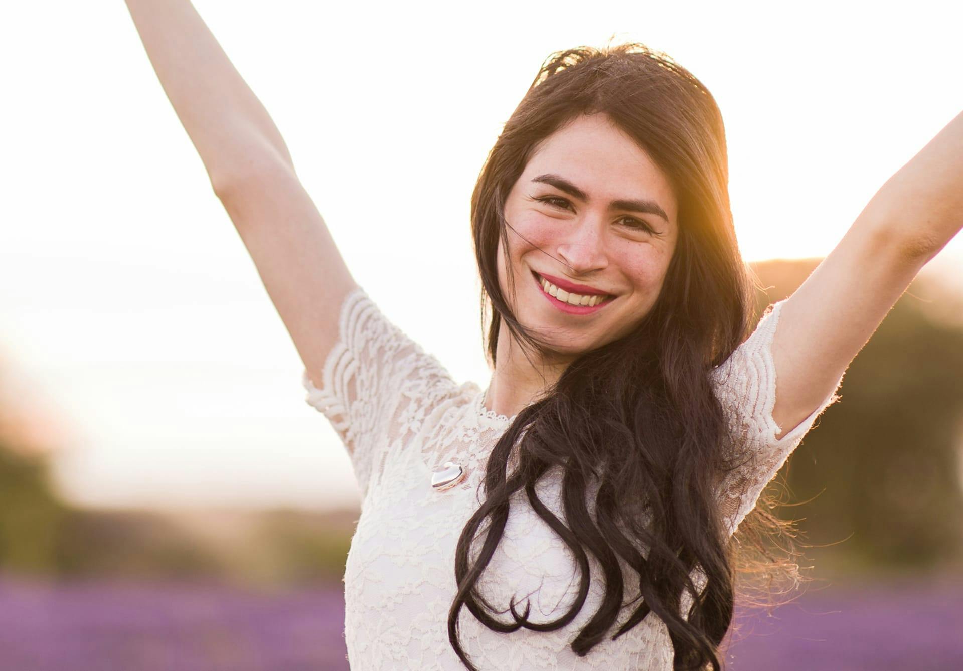 Woman with her hands up in the air outside smiling