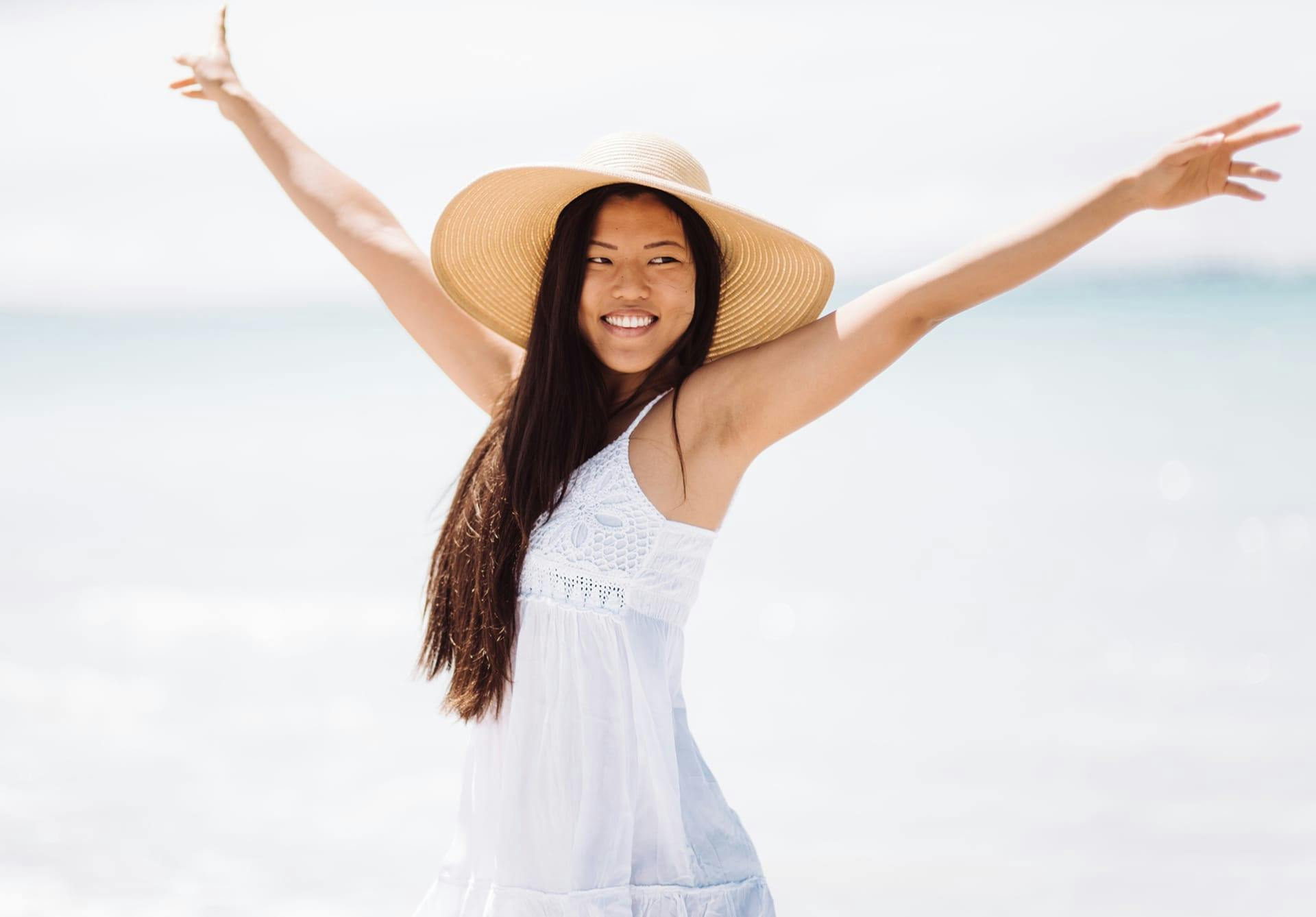 woman on beach with hat on and arms up
