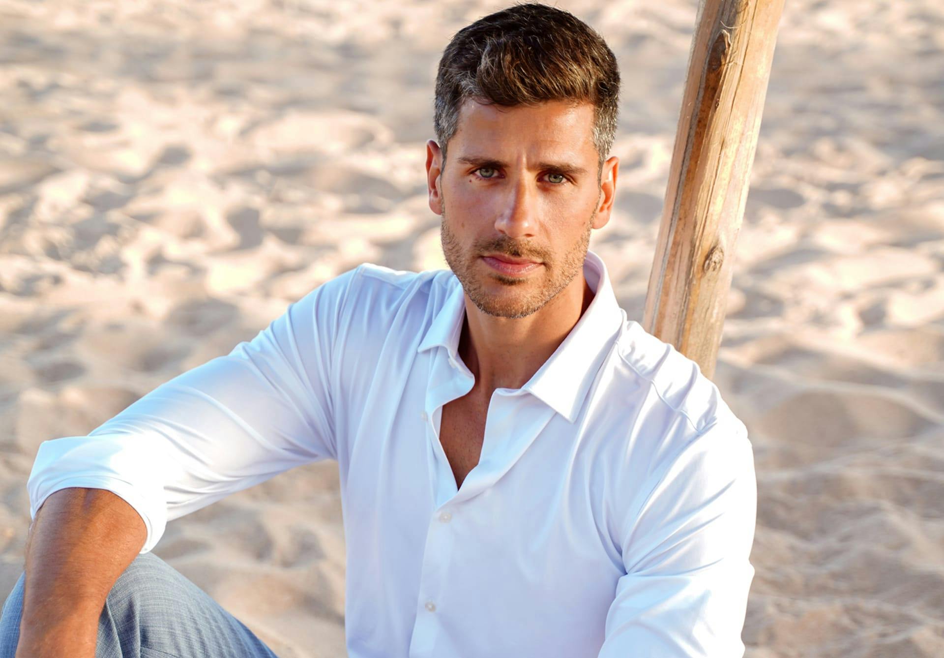 Handsome man in a white button up shirt sitting at the beach