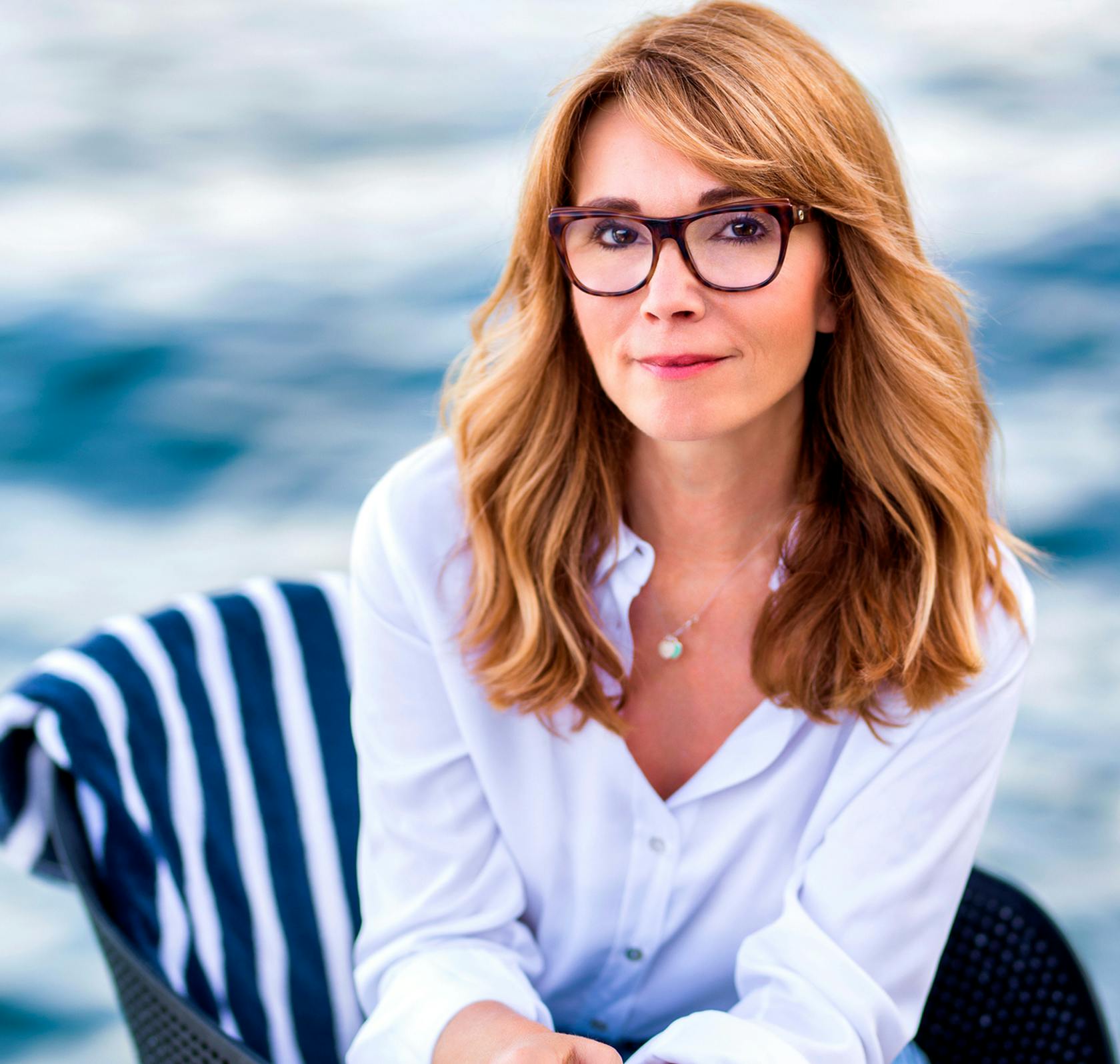 Woman with medium length copper hair wearing glasses, sitting by water