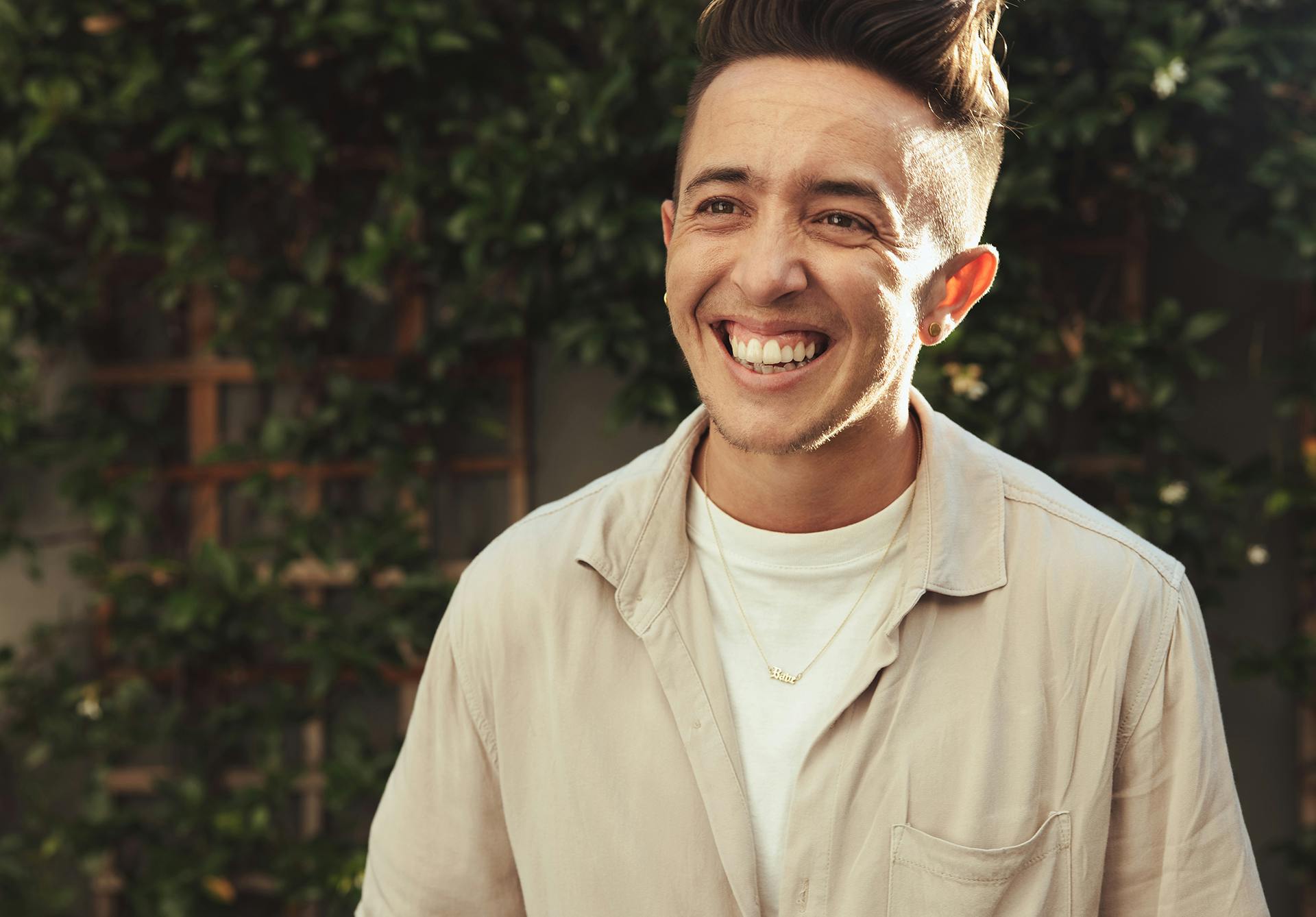 Person smiling wearing a beige button up over a white t-shirt