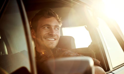 Man driving a car smiling with the sun setting behind him