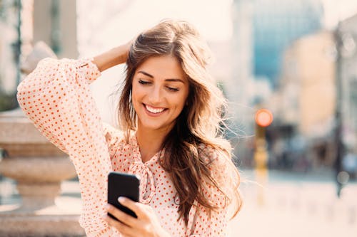 woman smiling outside while on her phone