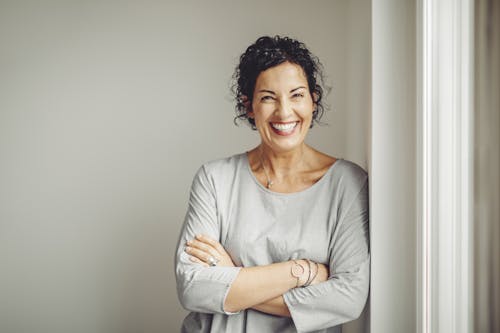 woman in a grey top smiling with her arms crossed