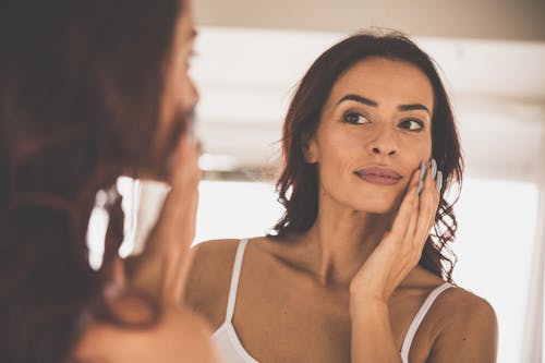 woman looking in the mirror while touching her face