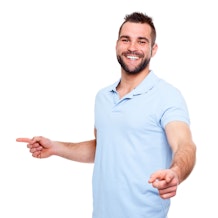 Ein lächelnder Mann in einem hellblauen Polohemd und Jeans steht vor einem weißen Hintergrund und zeigt mit beiden Händen auf etwas außerhalb des Bildes.