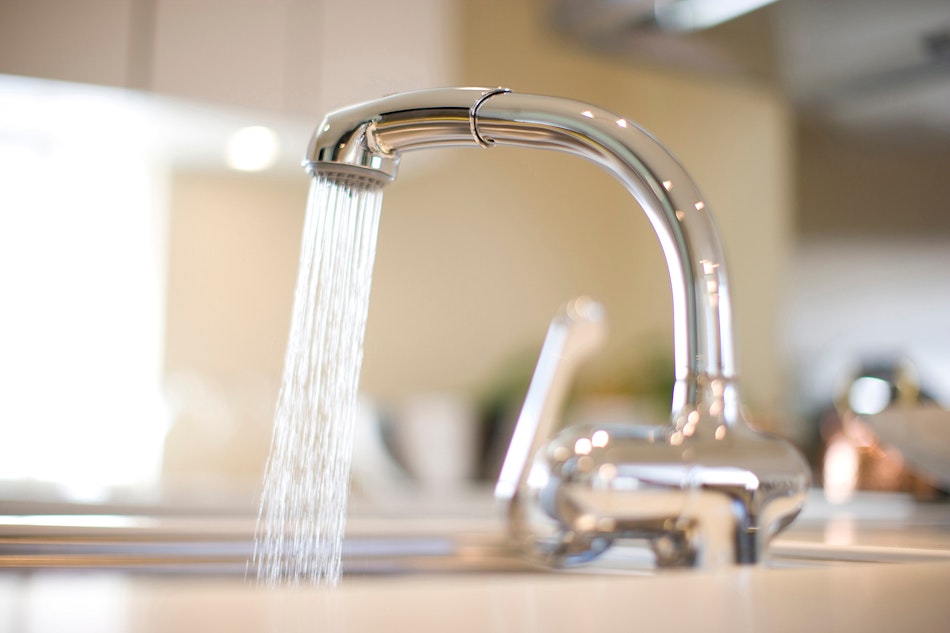 Wasserhahn mit Trinkwasser in der Küche, Wasser fließt durch ihn hindurch in ein Spülbecken